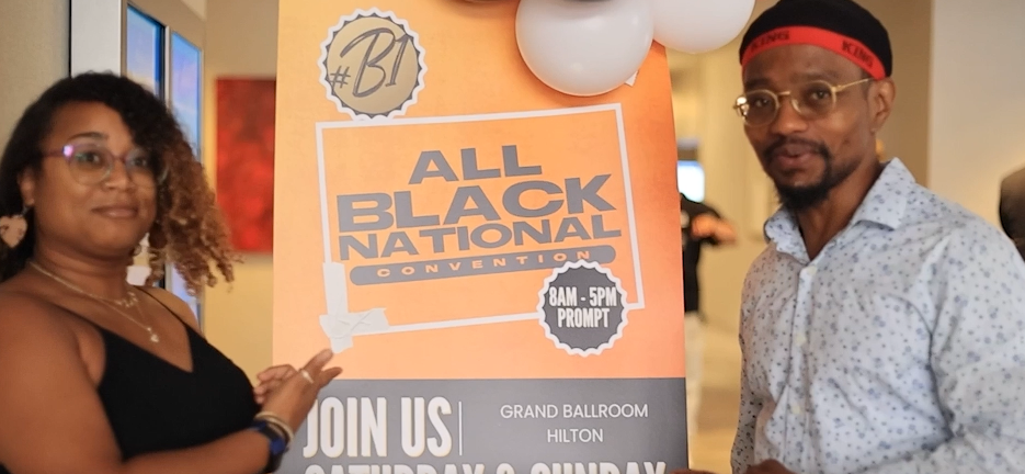 Two attendees posing next to the All Black National Convention welcome poster
